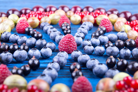 Ornament of assorted fruits and berries: gooseberries, raspberry, red and black currant, blueberry, sweet cherry. Blue wooden background. Selective focus.の写真素材