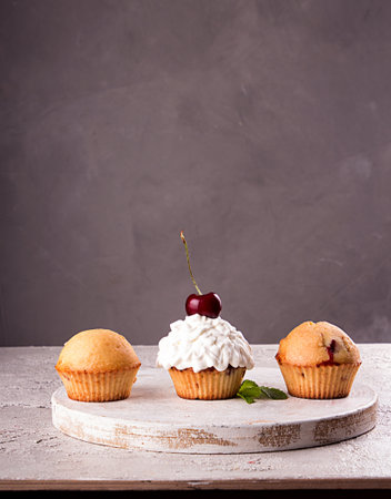 Muffins and cupkake with whipped cream decorated with strawberry on top on gray background. Copy spaceの写真素材