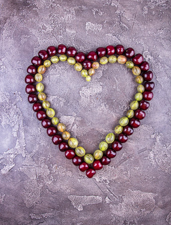 Fresh sweet cherries in heart shape over on grey concrete background. Top view. Copy space.