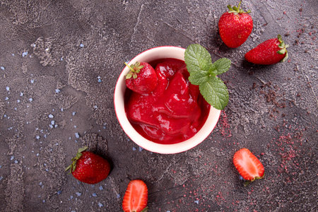 Strawberry sorbet in bowl and fresh berries. Summer refreshing dessert over on dark background. Top...