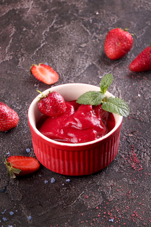 Strawberry sorbet in red bowl and fresh berries. Summer refreshing dessert over on dark background.の写真素材
