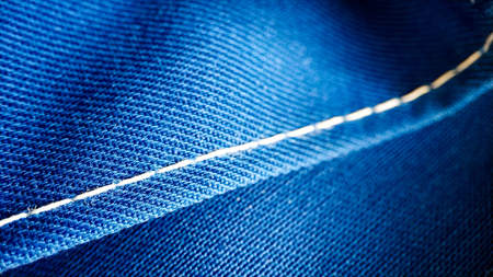 Texture of blue working clothes with white stitching closeup