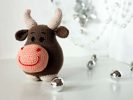 Crochet soft toy brown bull. The symbol of the new year 2021. On white background and silver Christmas decorations.の写真素材