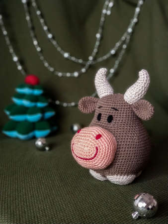 The symbol of the new year 2021. Knitted brown soft toy bull with horns. On green background and silver Christmas decorations.の写真素材
