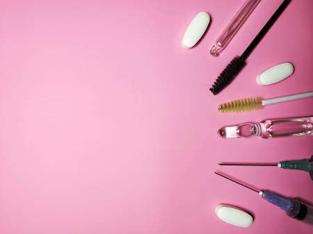 Medical cosmetology. Gloves, syringes, ampoule pills and brushes and eyebrows on a pink background side viewの写真素材