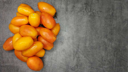 Lots yellow stretched long-fruited tomatoes on a gray stone background