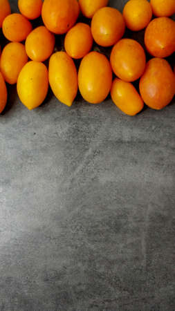 Lots yellow stretched long-fruited tomatoes on a gray stone background