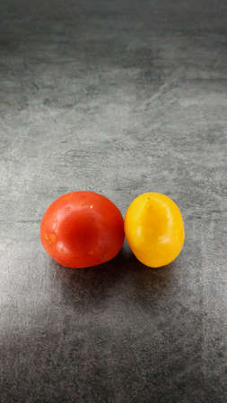 Pair of different tomatoes on a gray stone background. Yellow oblong and red round tomatoes.の写真素材