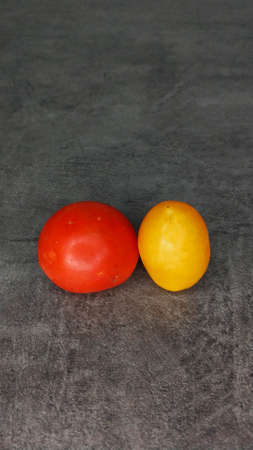 Pair of different tomatoes on a gray stone background. Yellow oblong and red round tomatoes.の写真素材