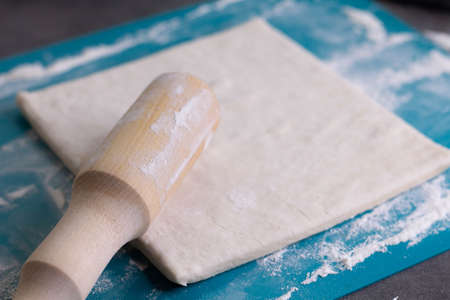 A piece of puff pastry and a wooden rolling pin on a turquoise boardの写真素材