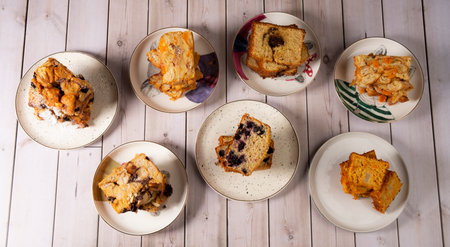 Group of four whole baked brown bread with raisins in ceramic plates on white wood