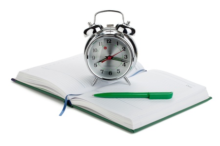 Alarm clock and pen on notepad. Isolated on white backgroundの写真素材