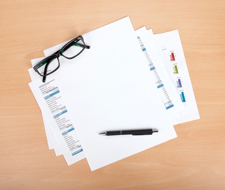Blank paper with pen and glasses over financial documentsの写真素材