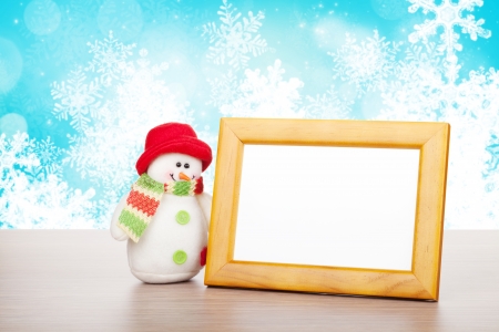 Blank photo frame and christmas snowman on wooden table over blue christmas backgroundの写真素材