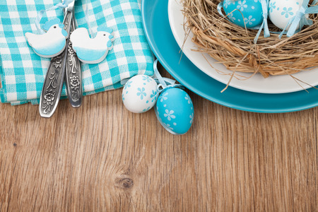 Easter eggs nest on plate over wooden background with copy space