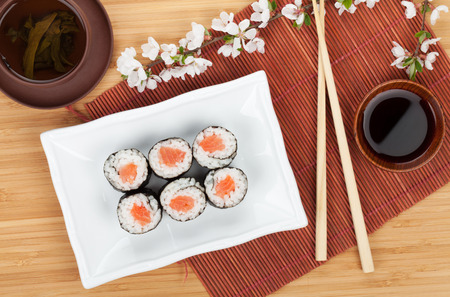 Japanese roll with salmon and fresh sakura branch over bamboo table and matの写真素材