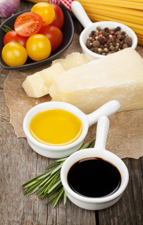 Parmesan cheese, pasta, tomatoes, vinegar, olive oil, herbs and spices on wooden table の写真素材