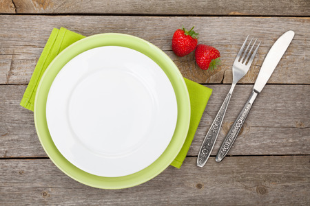 Empty plate with silverware and ripe strawberry over old wooden tableの写真素材