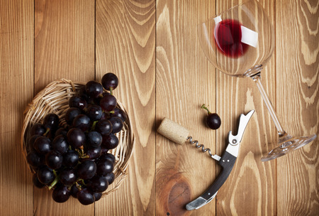 Red wine glass, corkscrew and grape on wooden table backgroundの写真素材