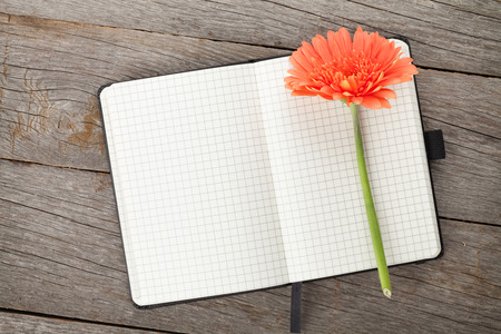 Blank notepad and orange gerbera flower on wooden table backgroundの写真素材