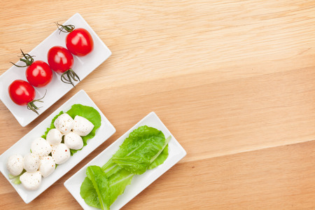Tomatoes, mozzarella and green salad leaves on wooden table backgroundの写真素材
