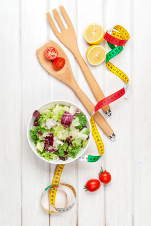 Fresh healthy salad, utensils and tape measure over white wooden table. View from aboveの写真素材