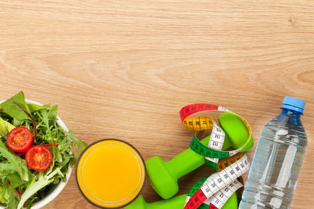 Dumbells, tape measure and healthy food over wooden background. Fitness and health. View from above with copy spaceの写真素材