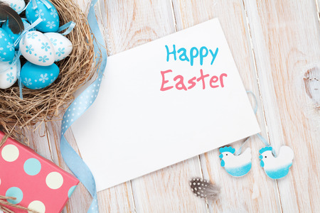 Easter greeting card with blue and white eggs and gift box over white wood. Top view with copy space