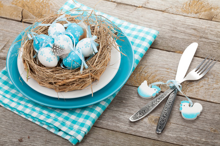 Easter eggs nest on plate over wooden background with silverware