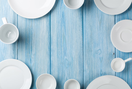 Empty plates and bowls on blue wooden background. Top view with copy space