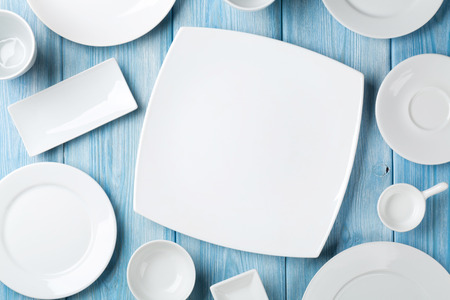 Empty plates and bowls on blue wooden background. Top view with copy space