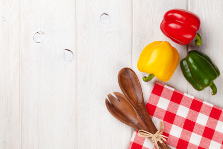 Colorful bell peppers and kitchen utensil on white wooden table. Top view with copy space