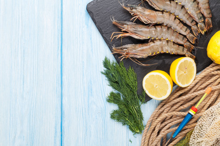 Fresh raw tiger prawns and fishing equipment on wooden table. Top view with copy spaceの写真素材