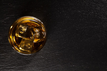 Glass of whiskey with ice on black stone table. Top view with copy spaceの写真素材