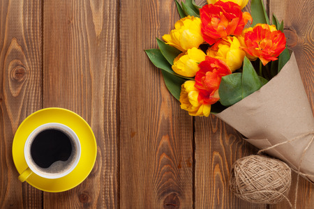 Colorful tulips bouquet and coffee cup on wooden table. Top view with copy spaceの写真素材