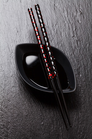Japanese sushi chopsticks over soy sauce bowl on black stone backgroundの写真素材