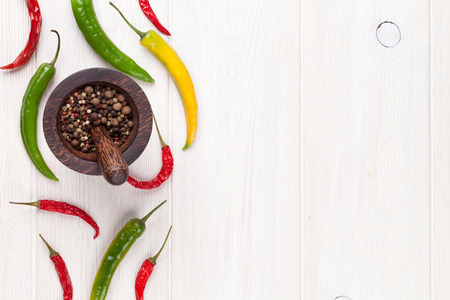 Colorful chili peppers and peppercorn on white wooden table. Top view with copy spaceの写真素材