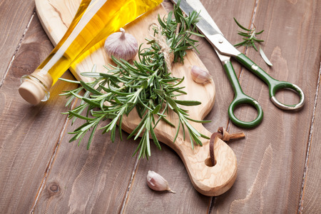 Fresh garden rosemary with garlic and olive oil on cutting board over wooden tableの写真素材