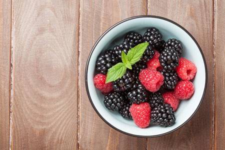 Blackberries and raspberries bowl on wooden table. Top view with copy space