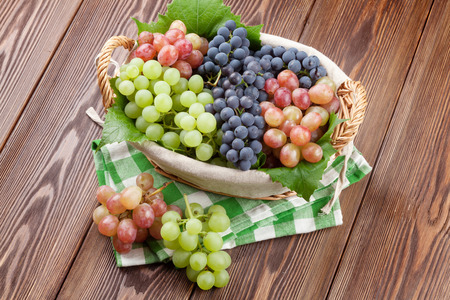 Bunch of red, purple and white grapes in basket on wooden table backgroundの写真素材