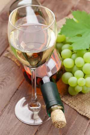 White wine glass, bottle and grapes on wooden tableの写真素材