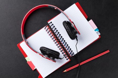 Headphones over notepad on black leather desk table. Top viewの写真素材