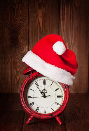 Christmas alarm clock with santa hat on wooden tableの写真素材
