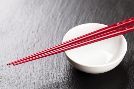 Japanese sushi chopsticks over soy sauce bowl on black stone background. Top view with copy spaceの写真素材