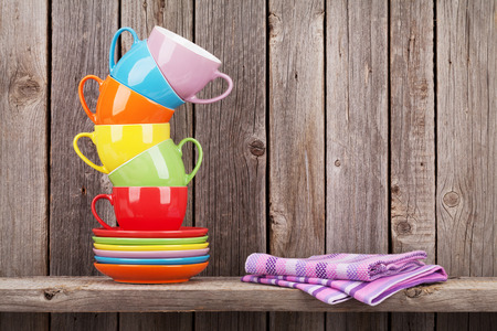 Colorful coffee cups on shelf against rustic wooden wall with copy spaceの写真素材