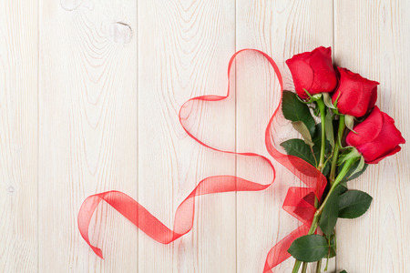 Red roses and heart shape ribbon over wooden table. Valentines day background. Top view with copy spaceの写真素材