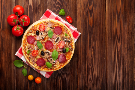 Italian pizza with pepperoni, tomatoes, olives and basil on wooden table. Top view with copy spaceの写真素材