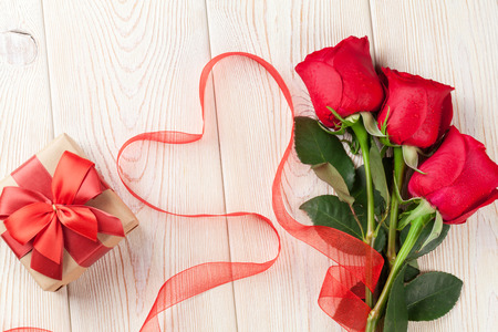 Red roses, Valentines day gift box and heart shaped ribbon over wooden backgroundの写真素材