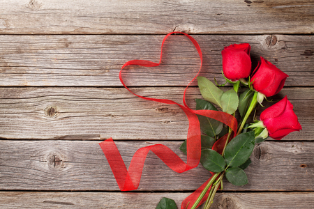 Red roses and heart shape ribbon over wooden table. Valentines day background. Top view with copy spaceの写真素材