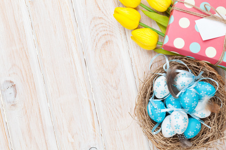 Easter background with blue and white eggs in nest, yellow tulips and gift box. Top view with copy...
